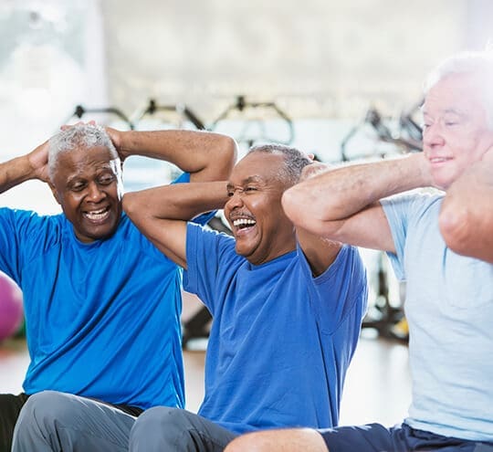 Three senior men in fitness room working out and laughing